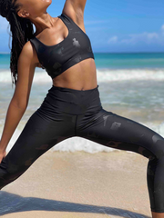 Model wearing Lukafit squat-proof legging and sports bra in Black on Black color. Photo is of the model doing a Reverse Warrior yoga pose on a beach.