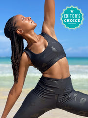 Photo of model doing a yoga pose on the beach in Black-Owned Lukafit activewear. Model is wearing squat-proof black leggings and matching black sports bra.