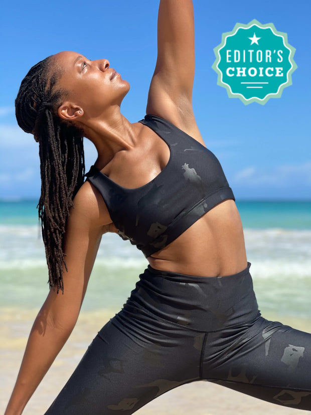 Photo of model doing a yoga pose on the beach in Black-Owned Lukafit activewear. Model is wearing squat-proof black leggings and matching black sports bra.